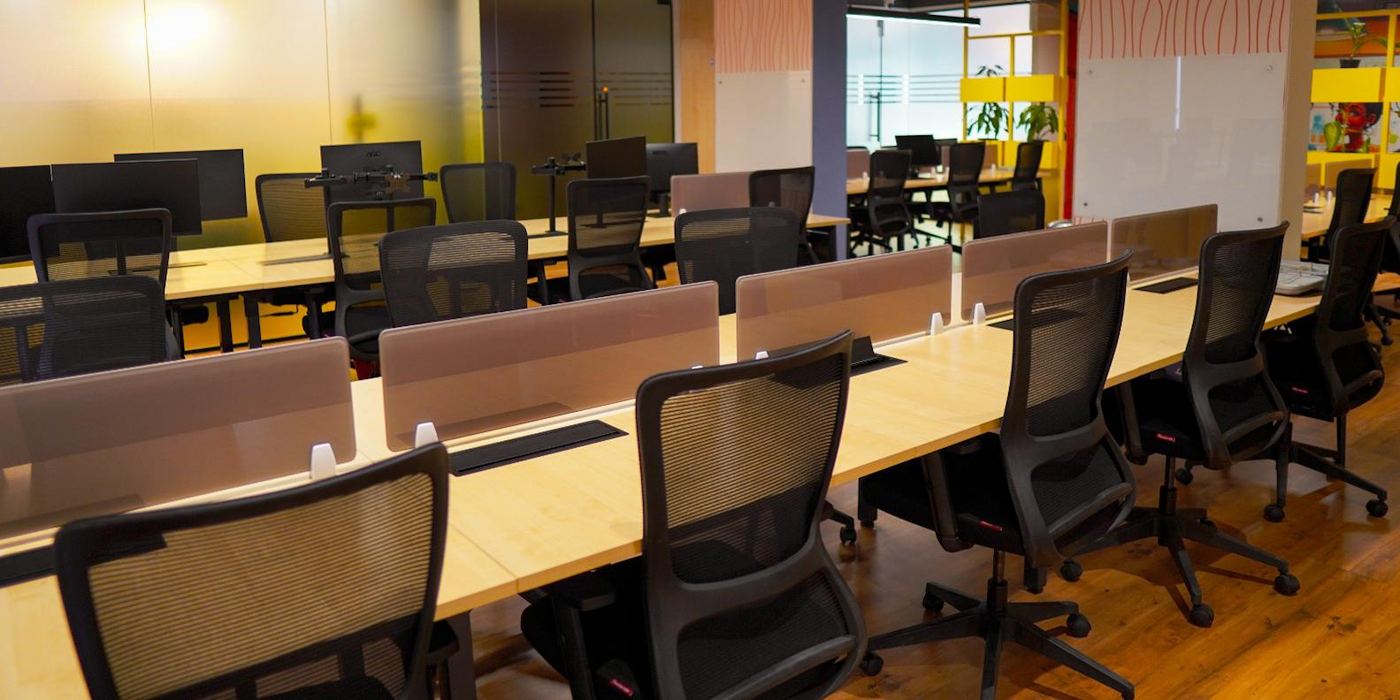 The QueWorkspace coworking floor: open desks with monitor arms and privacy screens